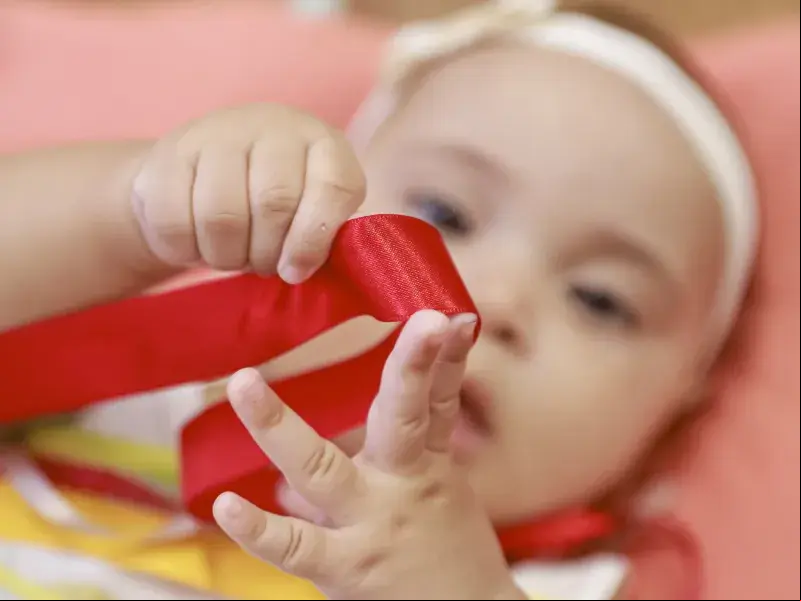Bebê brinca com laço de fita vermelho